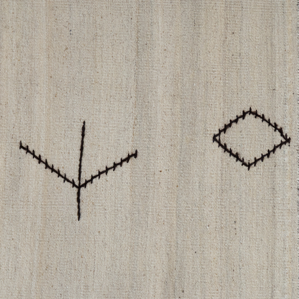 A close-up of a light beige woven fabric with two simple black stitched geometric motifs, one on the left and one on the right.