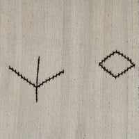 A close-up of a light beige woven fabric with two simple black stitched geometric motifs, one on the left and one on the right.