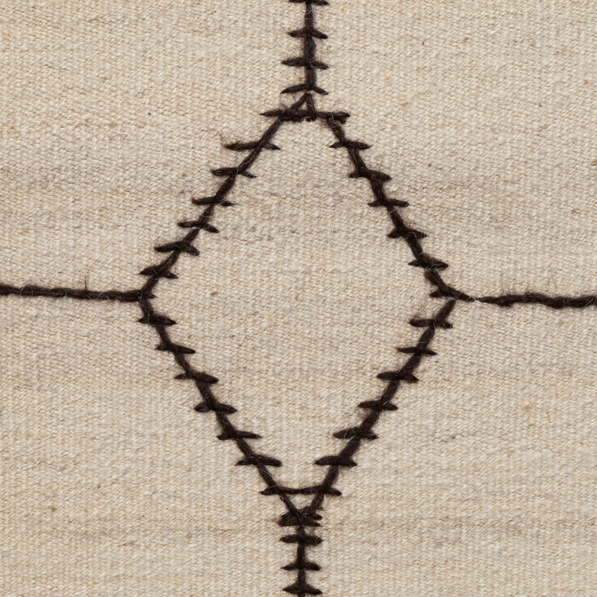 Close-up of a woven textile surface in warm beige with a dark brown geometric diamond and cross stitched pattern.