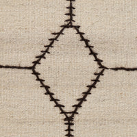 Close-up of a woven textile surface in warm beige with a dark brown geometric diamond and cross stitched pattern.