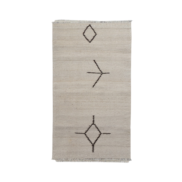 A rectangular natural beige woven rug with a minimalist black geometric pattern of diamonds and lines, featuring short fringe on the top and bottom edges.
