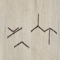 Close-up of a beige woven textile with three black embroidered geometric line motifs stitched on it.