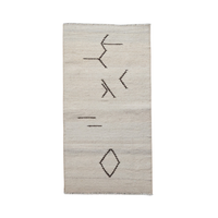A rectangular off-white woven rug with a minimalist black geometric pattern, including abstract lines and a diamond motif, shown against a plain white background.