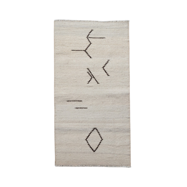 A rectangular off-white woven rug with a minimalist black geometric pattern, including abstract lines and a diamond motif, shown against a plain white background.