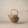 Ceramic teapot with a bamboo handle on a textured surface