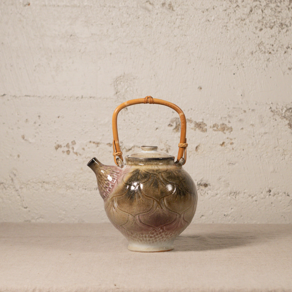 Ceramic teapot with a bamboo handle on a textured surface