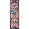 A long rectangular woven runner rug with a bold geometric tribal pattern in multiple colors including red, blue, black, beige, and white, shown flat against a white background.