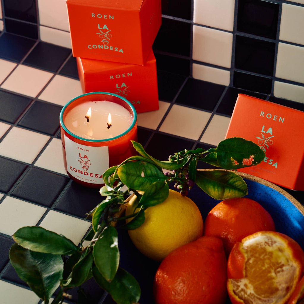 NUEVE LEONES Candle in orange displayed with fruit in a bowl 