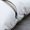 Close-up of a cream-colored fabric zippered cushion or pillow with a black zipper pull, resting on a rustic wooden surface.