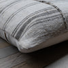 A close-up of a square throw pillow with a textured woven fabric in beige and gray stripes, resting on a rustic wooden floor.