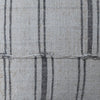 Close-up of woven fabric with a light beige base and vertical dark charcoal gray stripes, showing the textile texture and a horizontal stitched seam.