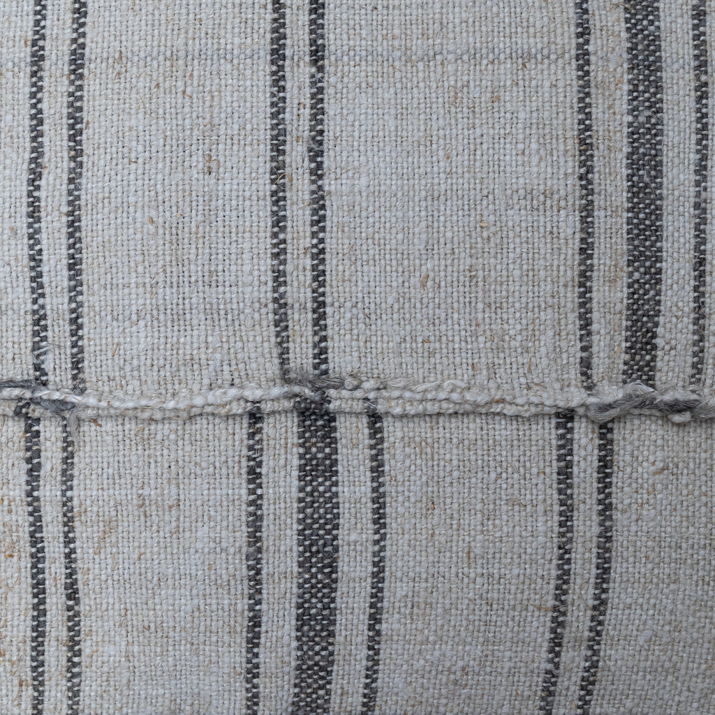 Close-up of woven fabric with a light beige base and vertical dark charcoal gray stripes, showing the textile texture and a horizontal stitched seam.