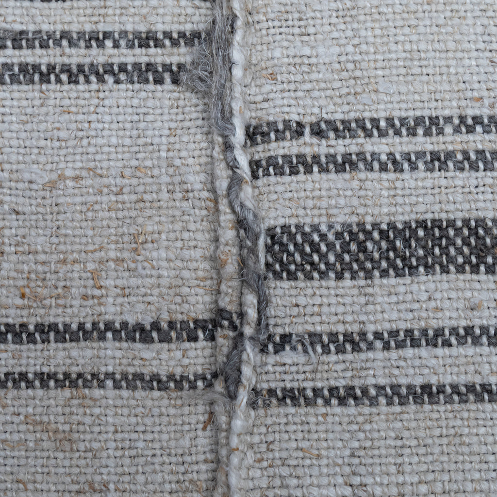 Close-up of a woven textile surface with a natural off-white base and dark charcoal gray horizontal stripes, showing the texture and weave detail.