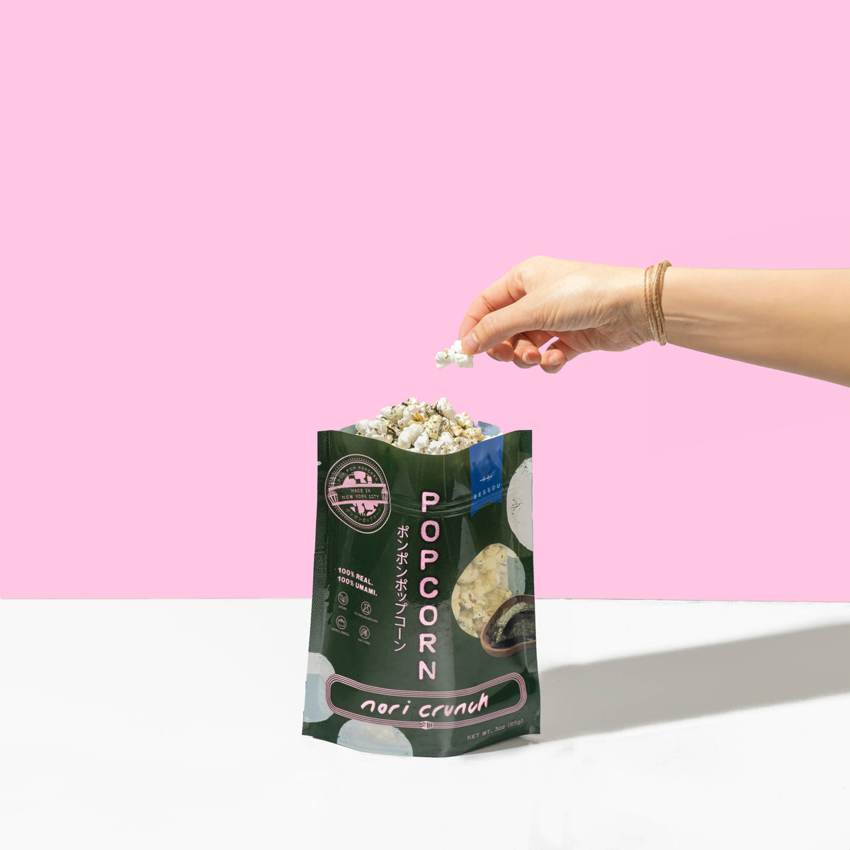 Hand holding a bag of popcorn with a pink background