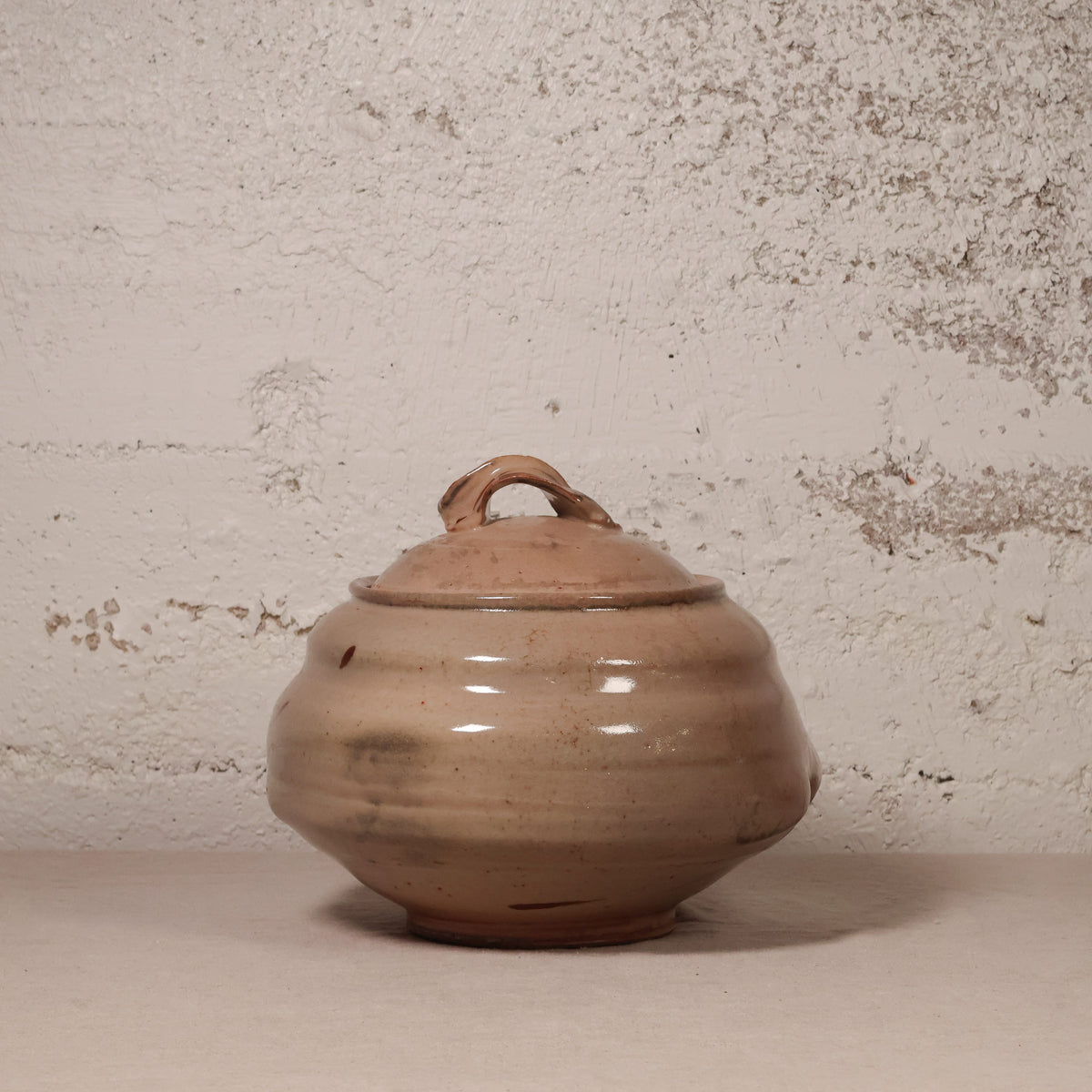 Brown ceramic jar with lid on a textured beige background