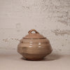 Brown ceramic jar with lid on a textured beige background