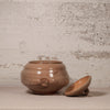Brown ceramic jar with lid on a textured surface and background