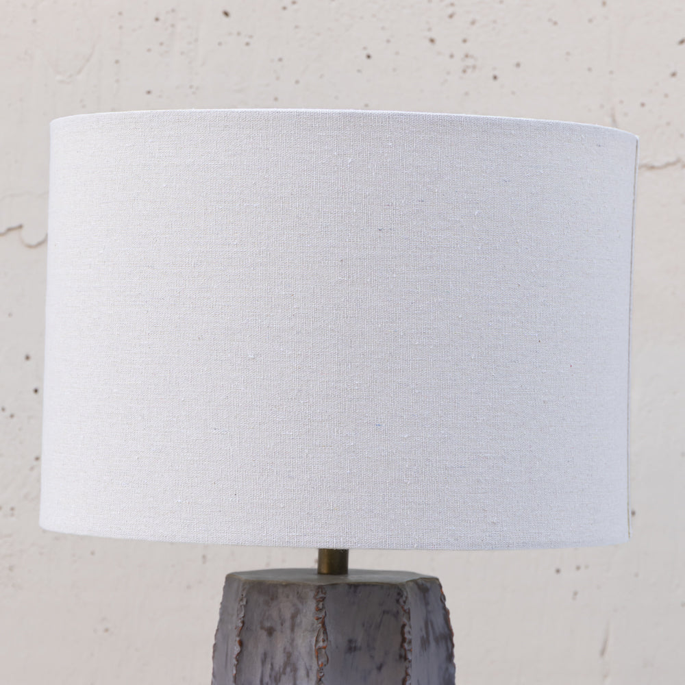 A table lamp with a large white fabric drum shade and a textured gray stone base, shown against a light neutral wall.