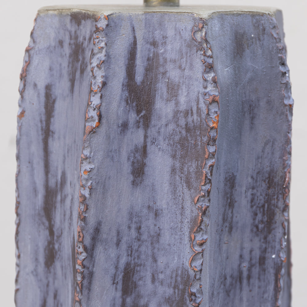 Close-up of a textured ceramic or stone-like surface with a distressed finish, showing vertical fluted panels in muted blue-gray with brown and orange weathered detailing.