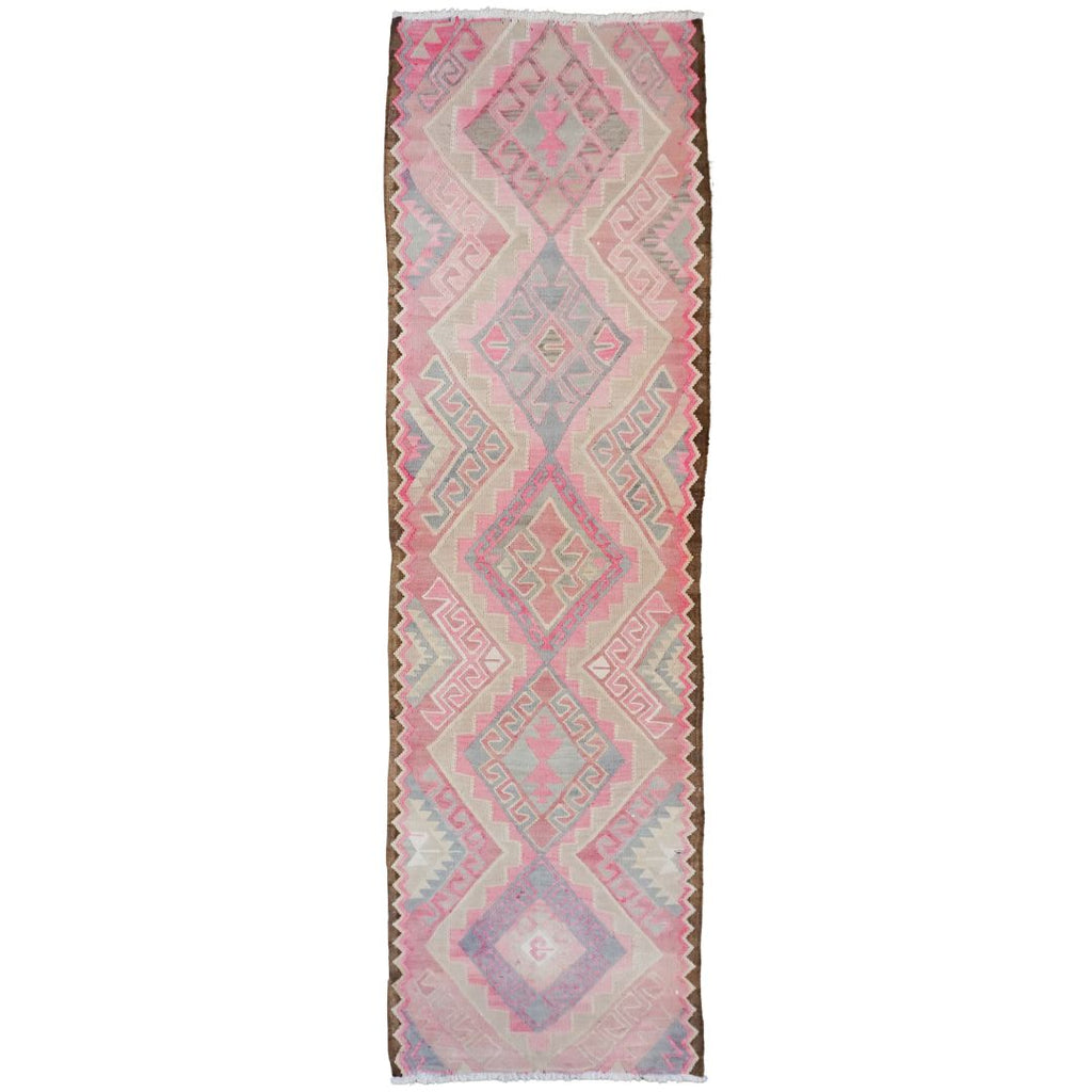 A long rectangular runner rug with a vintage geometric kilim pattern in shades of pink, beige, and light blue on a white background.