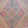 A close-up of a woven textile with a geometric kilim-style pattern in pink, beige, and gray.