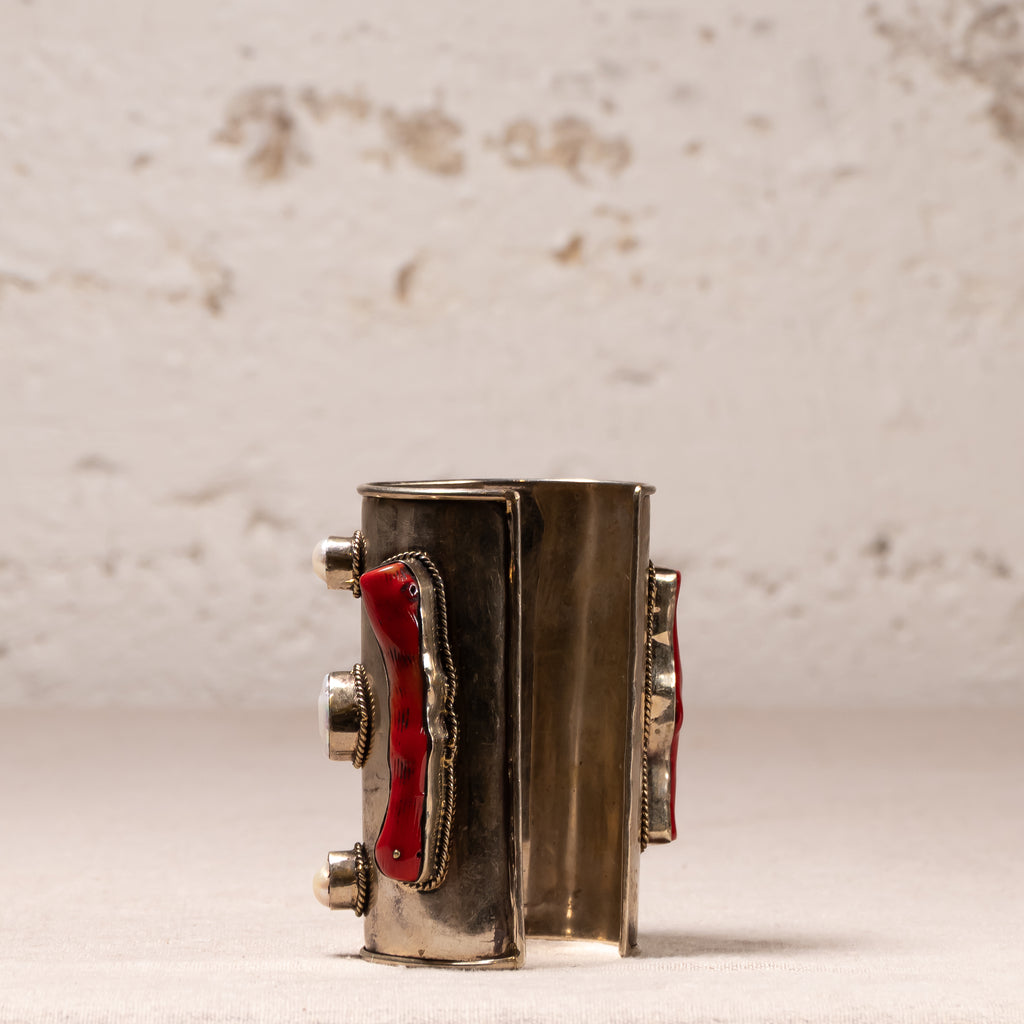 A vintage silver-toned cuff bracelet with red enamel inlays and silver-toned metal accents, displayed on a light textured surface against a neutral background.