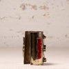 A vintage silver-toned cuff bracelet with red inlay details, standing upright on a light beige textured surface against a matching light beige background.