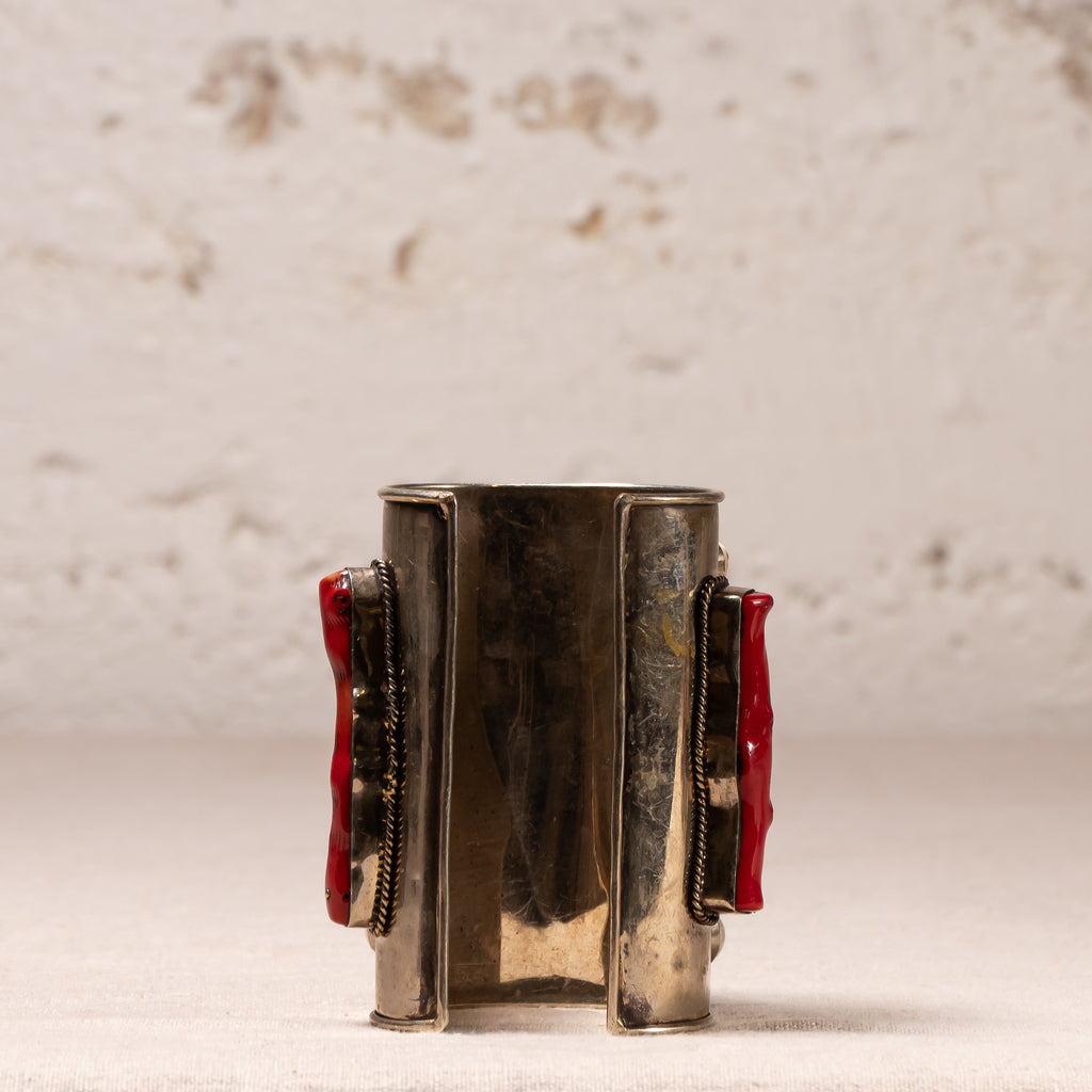 A vintage silver-toned cuff bracelet with red textured inlay panels on both sides, displayed against a textured off-white background.