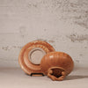 A handmade terracotta clay ceramic bowl with a matching saucer, displayed on a small black stand against a textured, distressed plaster wall.