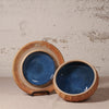 Two ceramic bowls with blue interior and brown exterior on a textured surface.