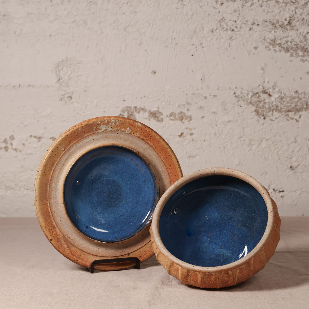 Two ceramic bowls with blue interior and brown exterior on a textured surface.