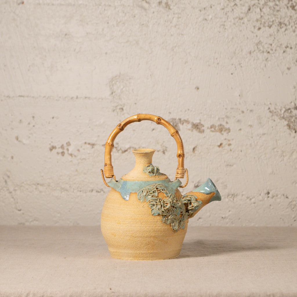 Ceramic teapot with bamboo handle on a textured surface
