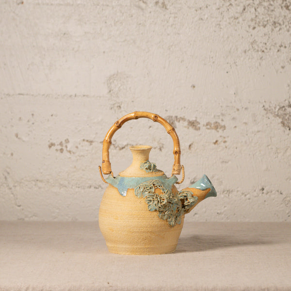 Ceramic teapot with bamboo handle on a textured surface