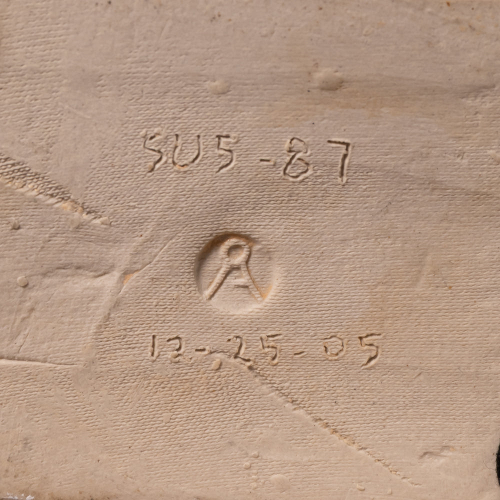 Close-up of a textured beige fabric or canvas surface with embossed or stitched markings including the numbers 'SU5-87' and '12-25-05' plus a circular emblem.