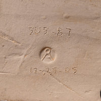 Close-up of a textured beige fabric or canvas surface with embossed or stitched markings including the numbers 'SU5-87' and '12-25-05' plus a circular emblem.
