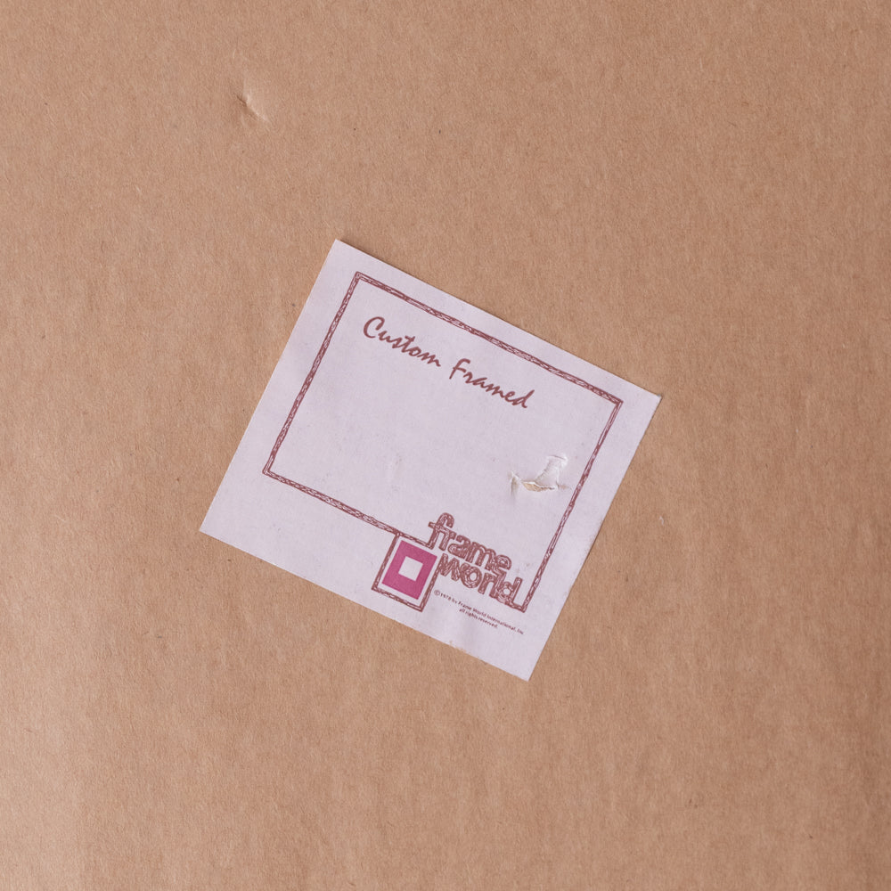 A small white square card with a pink border and the words 'Custom Framed' and the frame world logo, placed on a brown kraft paper background.