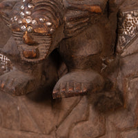 Close-up of a carved wooden sculpture with a dark brown finish and metallic silver accents on the face and side details.