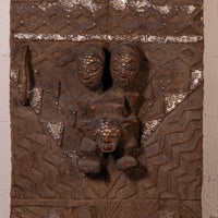 An antique carved wooden door panel featuring two human figures and a central animal head, detailed with geometric patterns and metallic silver-painted accents.