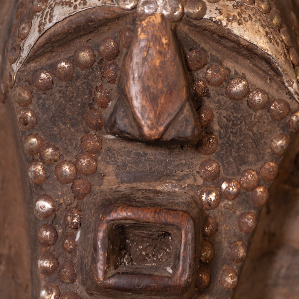 Close-up of a rustic bronze metal object with a textured surface, raised circular studs, and a central square recessed detail.