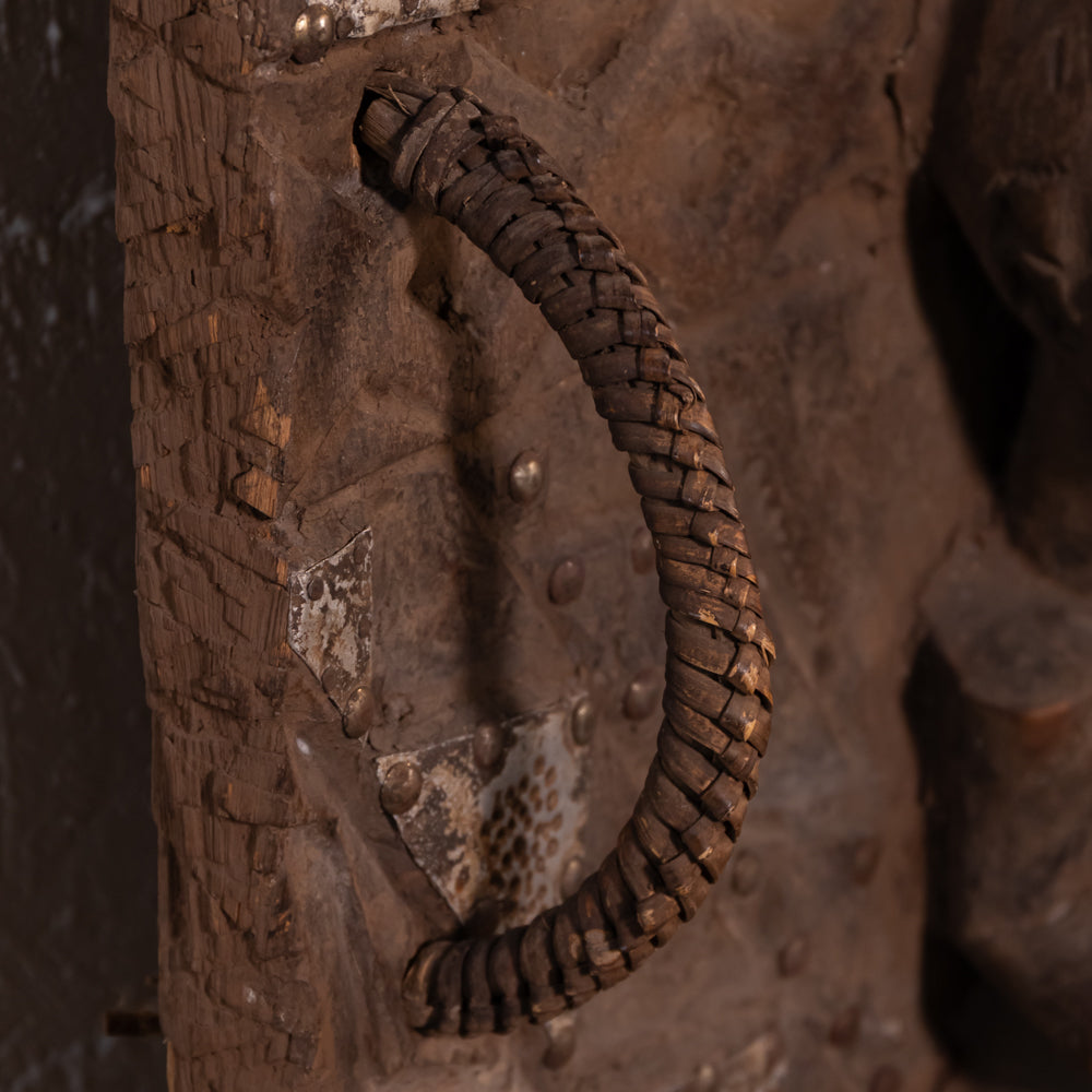 A close-up of a dark brown woven rope handle mounted on a rustic, textured brown wooden or metal door.