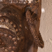 Close-up of a rustic brown metal doorbell with a braided leather pull cord, mounted against a textured light beige wall.