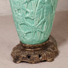 A close-up of a turquoise glazed ceramic vase with embossed floral relief patterns, resting on an ornate antique bronze metal base.