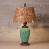 A vintage-style table lamp featuring a turquoise glazed ceramic vase base with embossed floral details, a natural woven seagrass lampshade, and dark bronze metal accents.