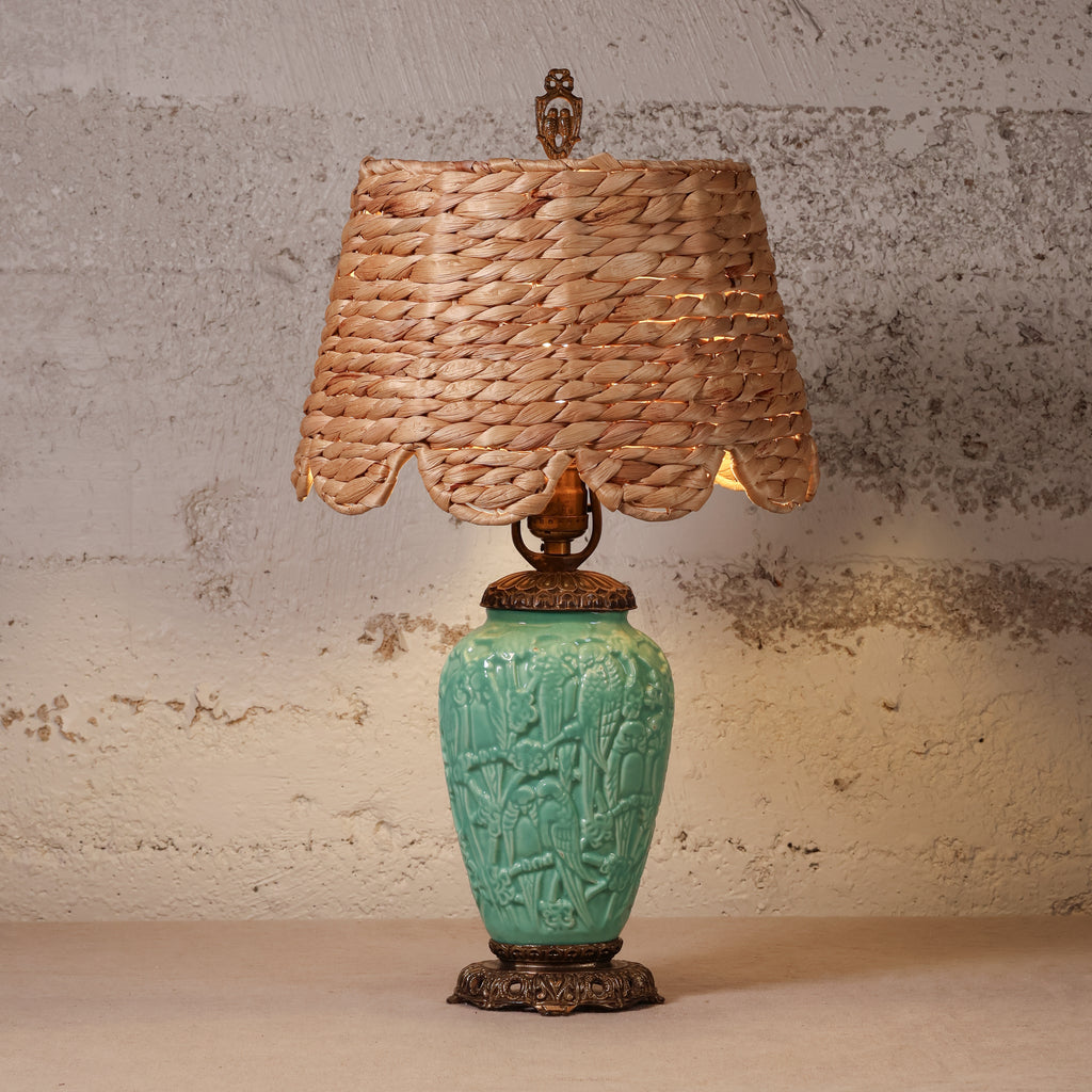 A vintage-style table lamp featuring a turquoise glazed ceramic vase base with embossed floral details, a natural woven seagrass lampshade, and dark bronze metal accents.