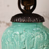 Close-up of a ceramic table lamp featuring a glossy turquoise-green relief-patterned body and a dark bronze metal collar and lamp base.