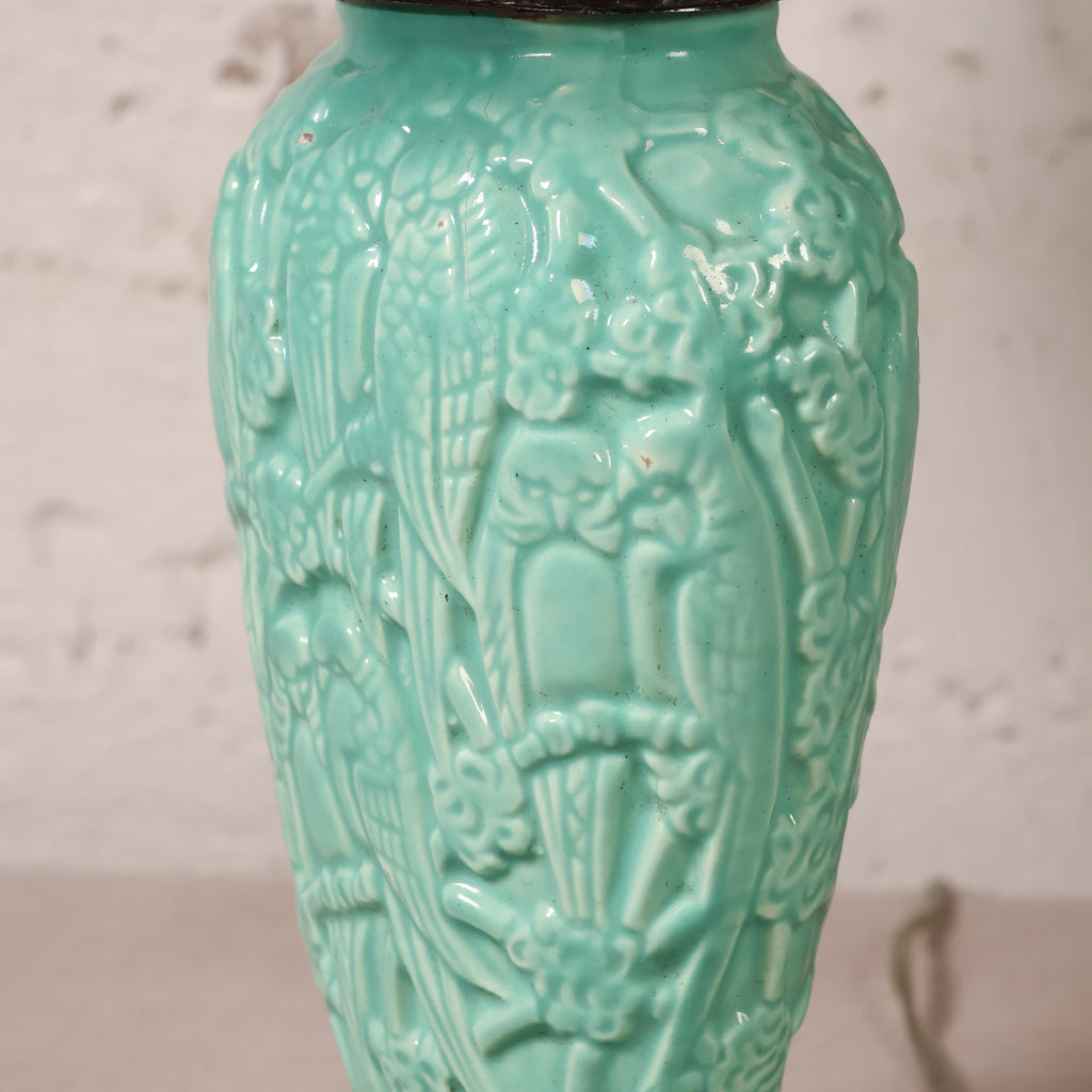 A close-up of a turquoise glazed ceramic vase featuring embossed relief carvings of birds and floral motifs, set against a light textured wall.