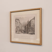 Framed black and white print of a city street scene on a beige wall.