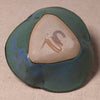 A handmade ceramic bowl with a rounded organic shape, featuring a glossy dark green and blue glazed exterior and a natural beige clay center with a brown painted signature.
