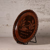 An oval dark brown wooden decorative tray with a carved swan and leaf design in the center, displayed on a black metal stand against a textured light gray wall.