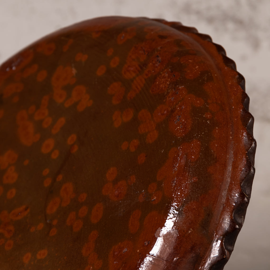 Close-up of a dark brown ceramic plate with a glossy finish and orange-brown mottled speckled pattern, showing a scalloped rim.